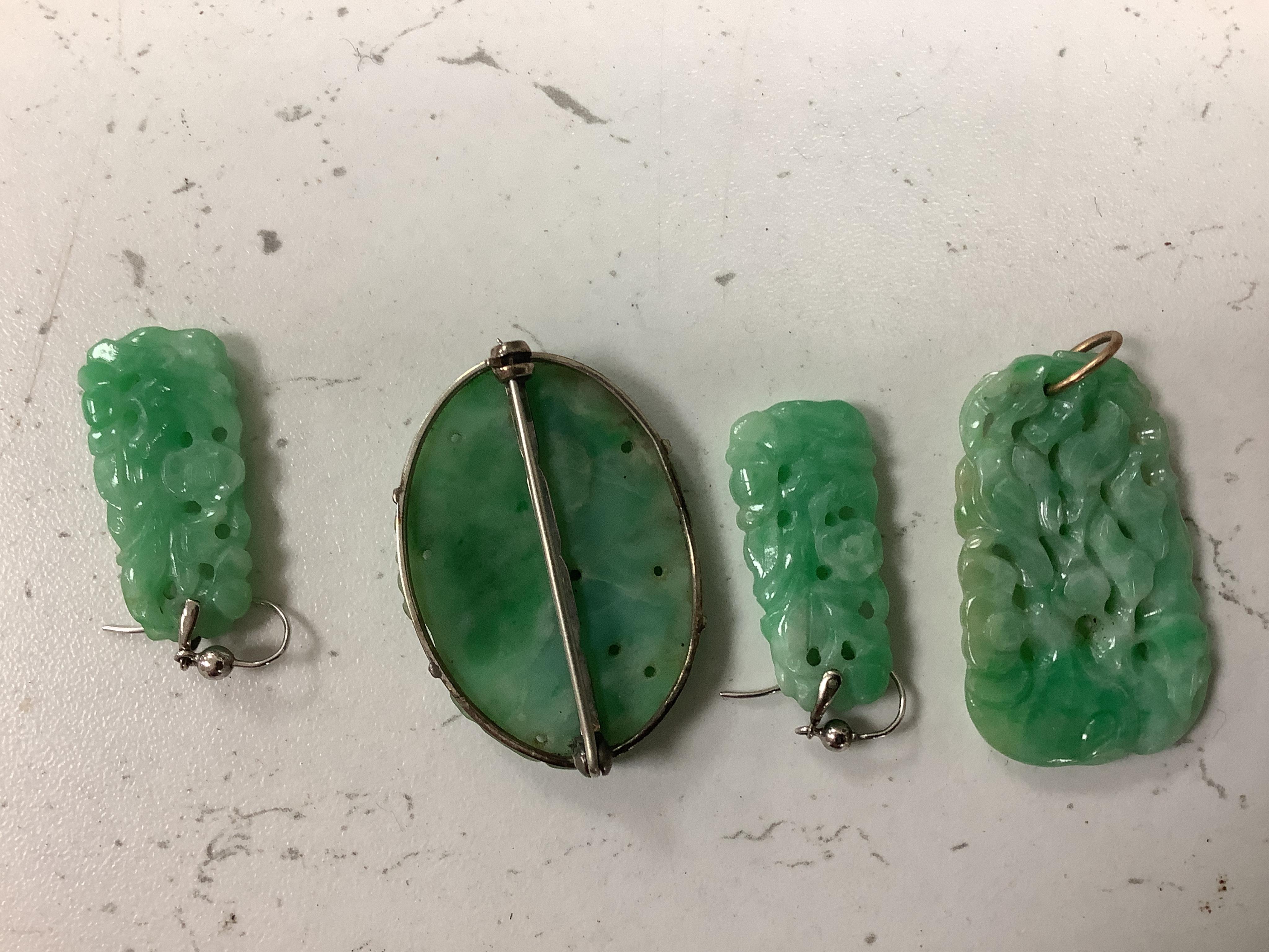 Four items of white metal mounted carved jade jewellery, comprising a brooch, 37mm, a pendant and pair of earrings.